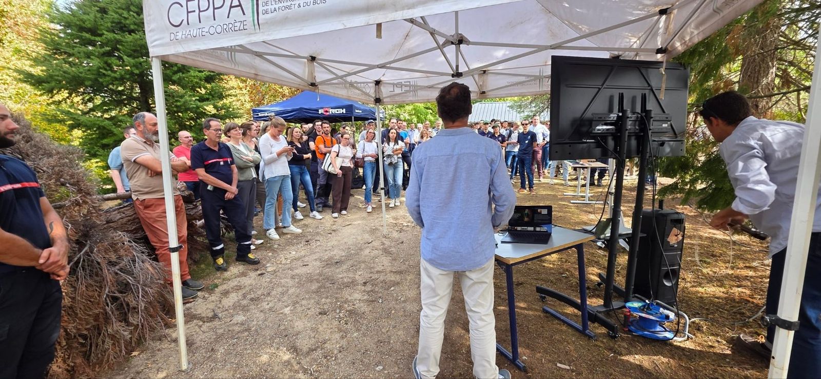 Visitantes bajo una carpa siguiendo la demostración en directo de detección de incendios forestales de SEBELO en Meymac